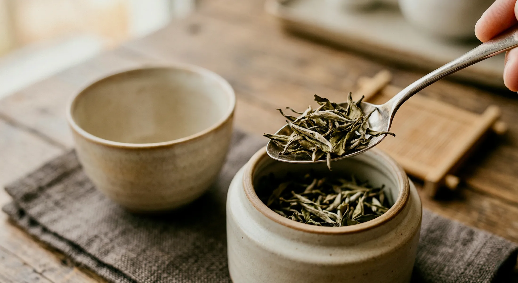 Colher com folhas de chá sobre um pote de cerâmica ao lado de uma xícara